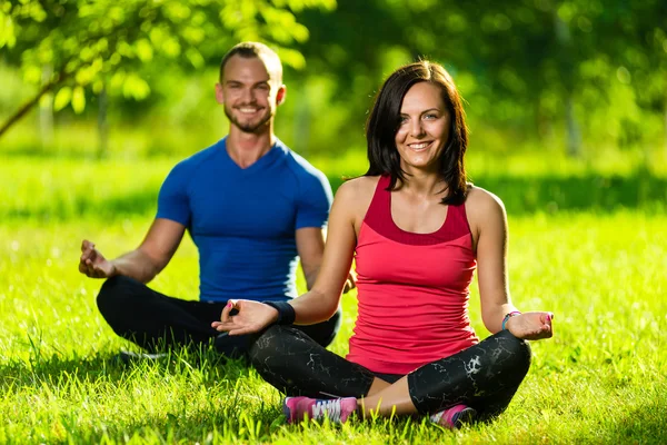 Hombre y mujer jóvenes haciendo yoga en el soleado parque de verano —  Fotos de Stock