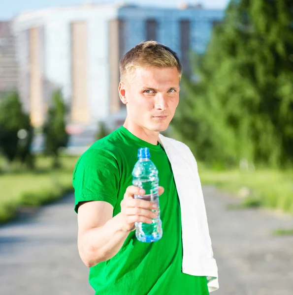 Tired man with white towel drinking water from a plastic bottle — Stock Photo, Image