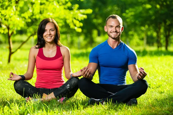 Jovem homem e mulher fazendo ioga no ensolarado parque de verão — Fotografia de Stock
