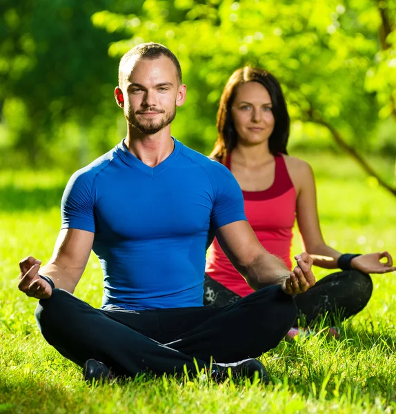 Genç adam ve kadın güneşli yaz parkta yoga yaparken — Stok fotoğraf