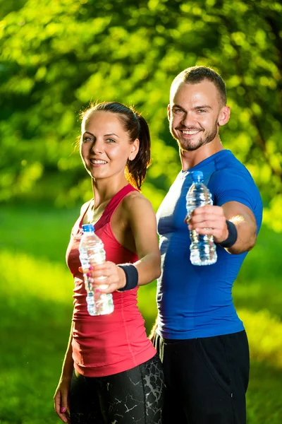 Uomo e donna che bevono acqua dalla bottiglia dopo l'esercizio fisico — Foto Stock