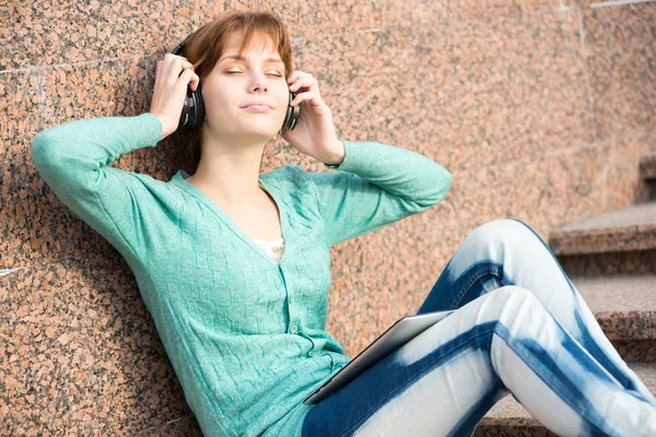 Mooie jonge vrouw student met een koptelefoon. Buiten muziek meisje — Stockfoto