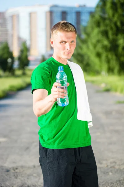 Trött man med vit handduk dricksvatten från en plastflaska — Stockfoto