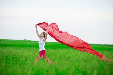 Young lady runing with tissue in green field. Woman and red scarf.