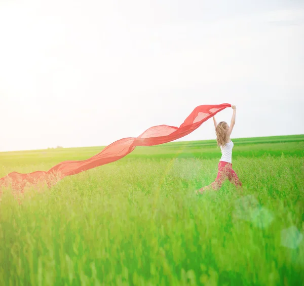 Giovane donna che corre con tessuto in campo verde. Donna e sciarpa rossa . — Foto Stock