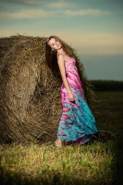 Jovem mulher em pé no campo da noite sobre palheiro. Moda pocilga — Fotografia de Stock