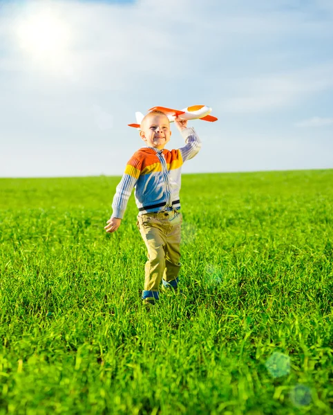 Niño feliz jugando con el avión de juguete contra el cielo azul de verano y el fondo verde del campo . — Foto de Stock