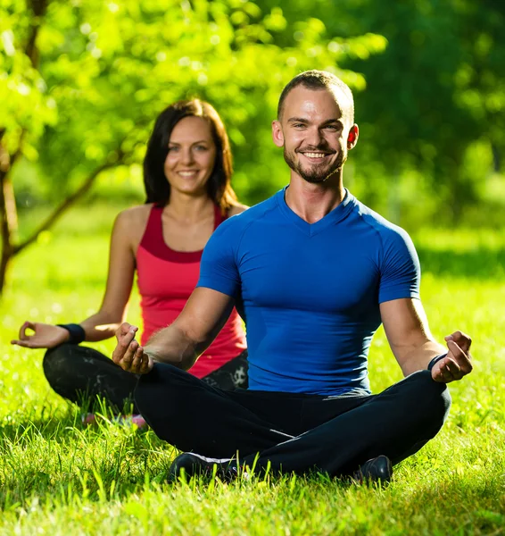 Hombre y mujer jóvenes haciendo yoga en el soleado parque de verano —  Fotos de Stock