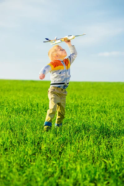 Felice ragazzo che gioca con aeroplano giocattolo contro cielo blu estate e sfondo campo verde . — Foto Stock