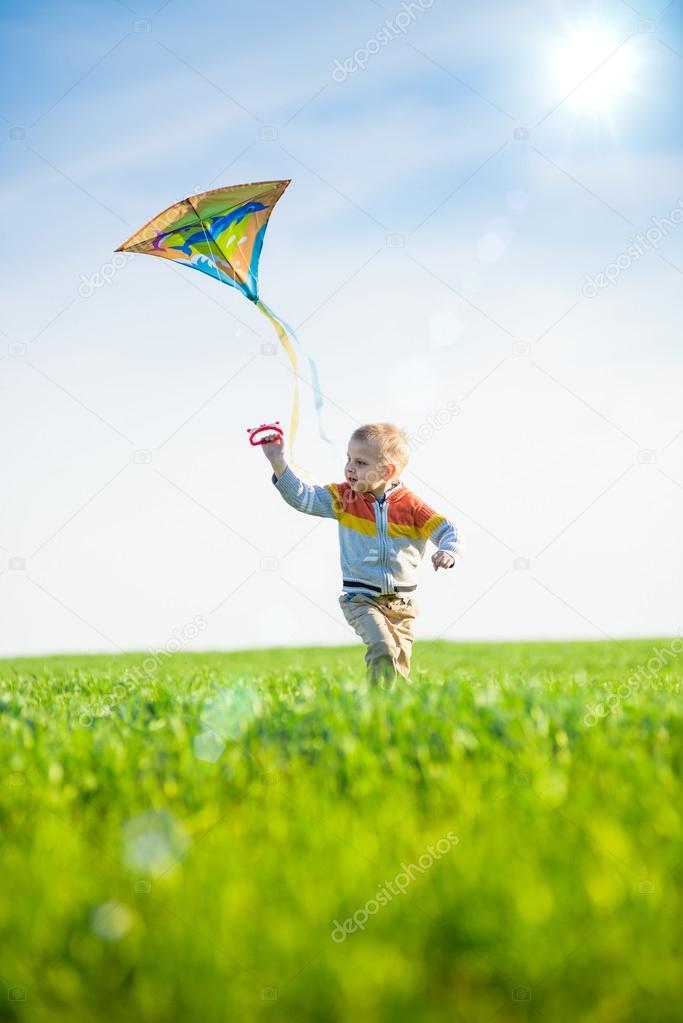 Young boy playing with his kite in a green field. 