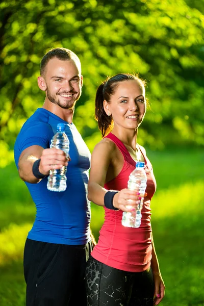 Uomo e donna che bevono acqua dalla bottiglia dopo l'esercizio fisico — Foto Stock