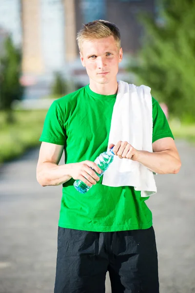 Trött man med vit handduk dricksvatten från en plastflaska — Stockfoto