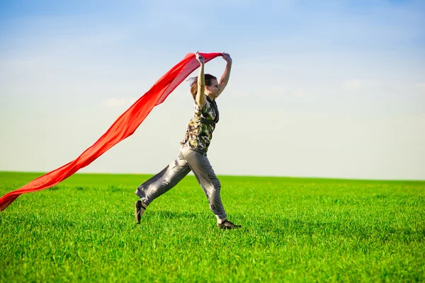 Hermosa mujer joven saltando en un prado verde con tejido de color — Foto de Stock