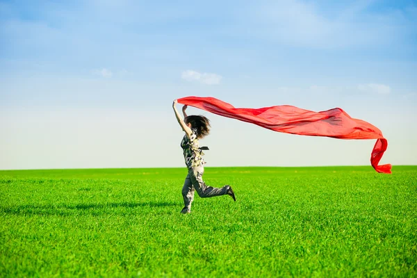 Hermosa mujer joven saltando en un prado verde con tejido de color — Foto de Stock