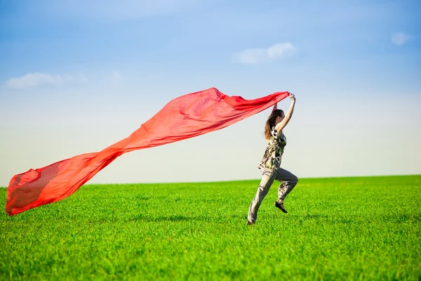 Beautiful young woman jumping on a green meadow with colored tissue — Stock Photo, Image