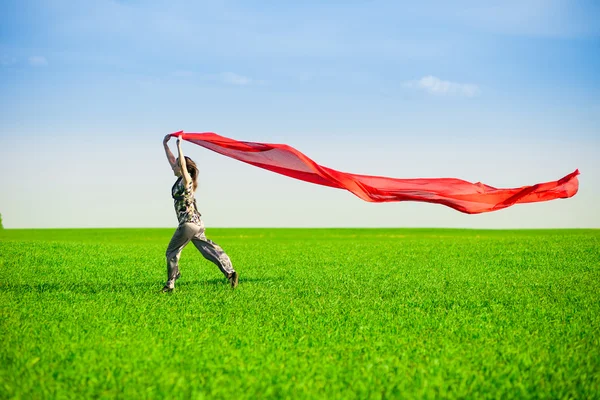 Beautiful young woman jumping on a green meadow with colored tissue — Stock Photo, Image