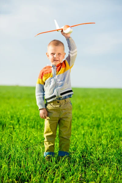 Happy boy playing with toy airplane against blue summer sky and green field background. — Stock Photo, Image