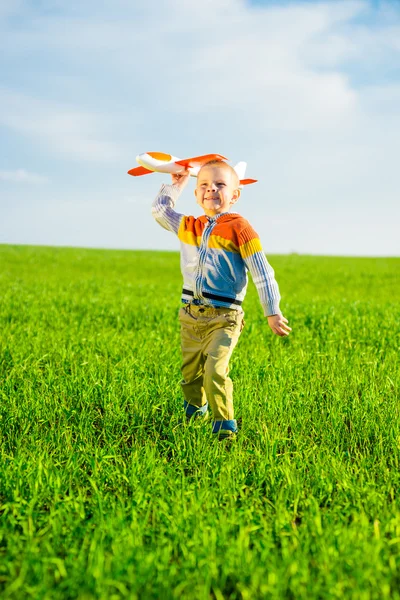 Felice ragazzo che gioca con aeroplano giocattolo contro cielo blu estate e sfondo campo verde . — Foto Stock