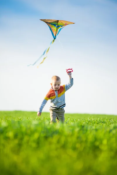 Niño jugando con su cometa en un campo verde . — Foto de Stock