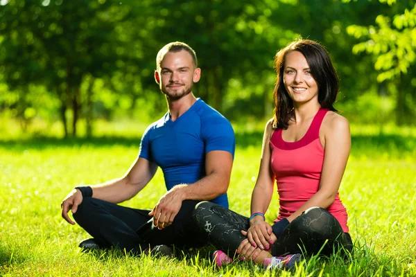 Young man and woman doing yoga in the sunny summer park — Stock Photo, Image