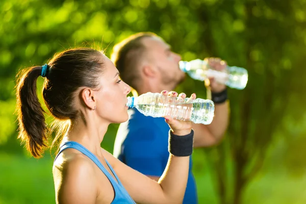 Мужчина и женщина пьют воду из бутылки после занятий спортом — стоковое фото