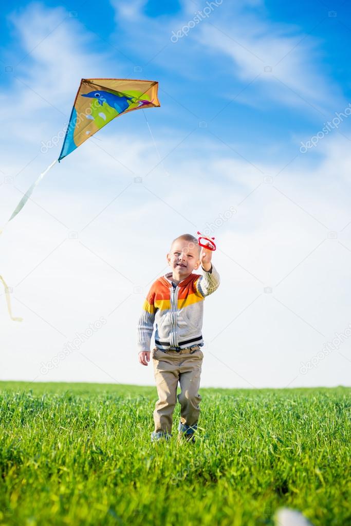 Young boy playing with his kite in a green field. 