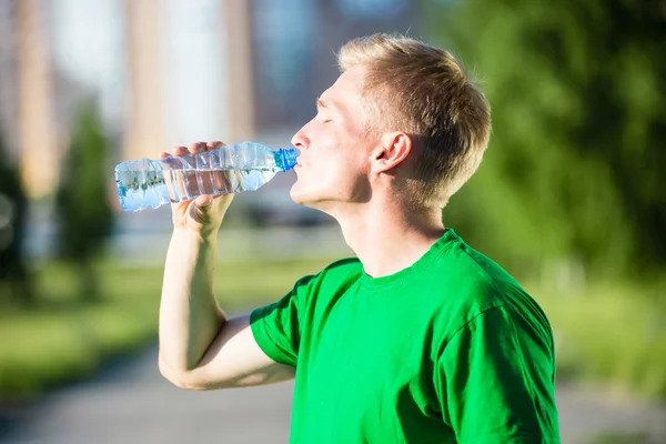 Trött man dricksvatten från en plastflaska efter fitness — Stockfoto