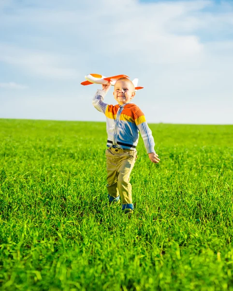 Felice ragazzo che gioca con aeroplano giocattolo contro cielo blu estate e sfondo campo verde . — Foto Stock