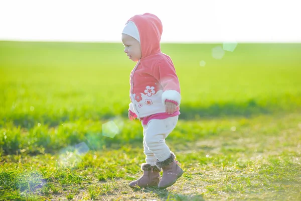 Glückliches kleines Mädchen, das auf der Wiese spaziert und in die Sonne schaut — Stockfoto
