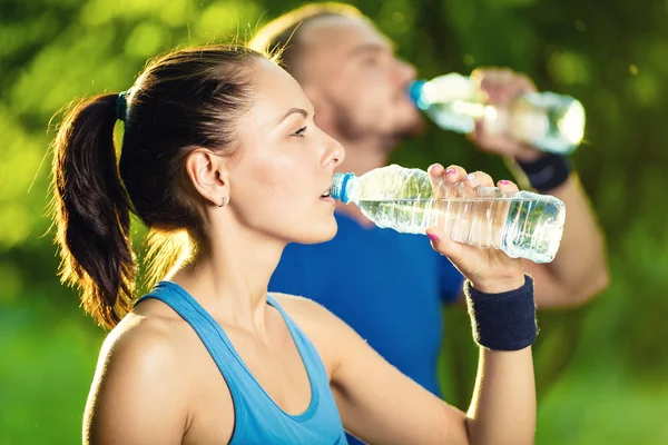 Чоловік і жінка п'ють воду з пляшки після спортивних вправ — стокове фото