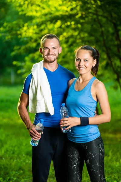 Άνδρας και γυναίκα πόσιμο νερό από το μπουκάλι μετά το γυμναστήριο αθλητισμού άσκηση — Φωτογραφία Αρχείου