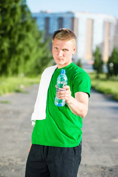 Hombre cansado con toalla blanca bebiendo agua de una botella de plástico — Foto de Stock