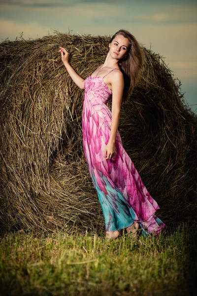Akşam alanında haystack üzerinde duran genç kadın. Moda arpacık — Stok fotoğraf
