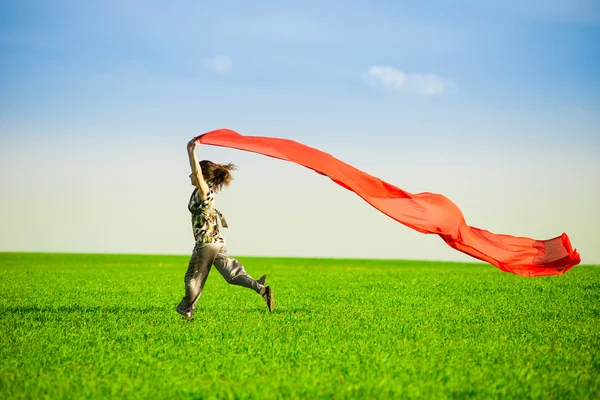 Beautiful young woman jumping on a green meadow with colored tissue — Stock Photo, Image