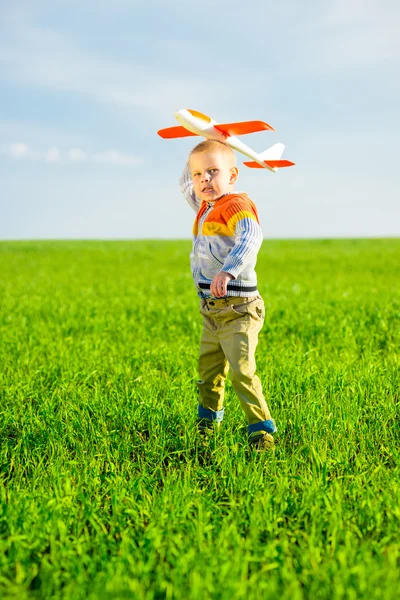 Felice ragazzo che gioca con aeroplano giocattolo contro cielo blu estate e sfondo campo verde . — Foto Stock