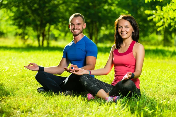 Hombre y mujer jóvenes haciendo yoga en el soleado parque de verano —  Fotos de Stock