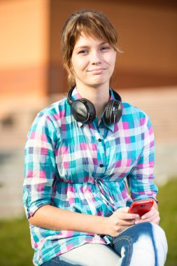 Gülümseyen genç kolej kız manifatura bir cep telefonu. Kampüs