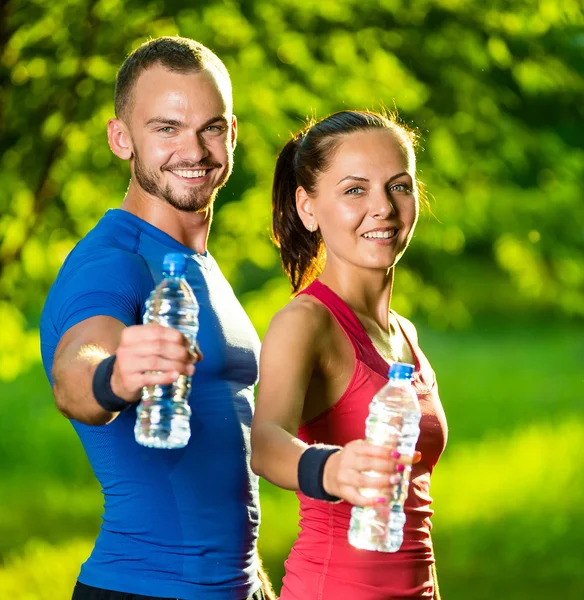 Uomo e donna che bevono acqua dalla bottiglia dopo l'esercizio fisico — Foto Stock