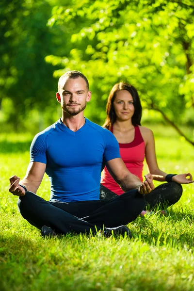 Hombre y mujer jóvenes haciendo yoga en el soleado parque de verano —  Fotos de Stock