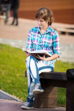 Öğrenci kızla defterini bankta. Yaz kampüs park.