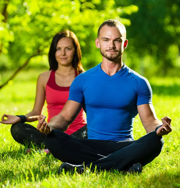 Hombre y mujer jóvenes haciendo yoga en el soleado parque de verano —  Fotos de Stock