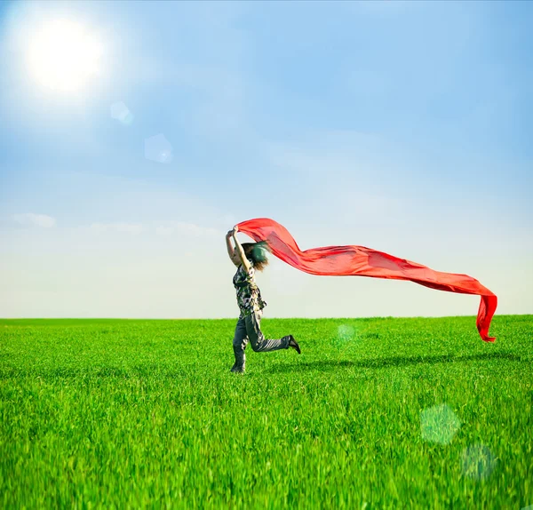 Hermosa mujer joven saltando en un prado verde con tejido de color —  Fotos de Stock