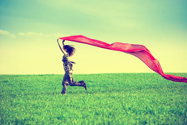 Beautiful young woman jumping on a green meadow with colored tissue — Stock Photo, Image