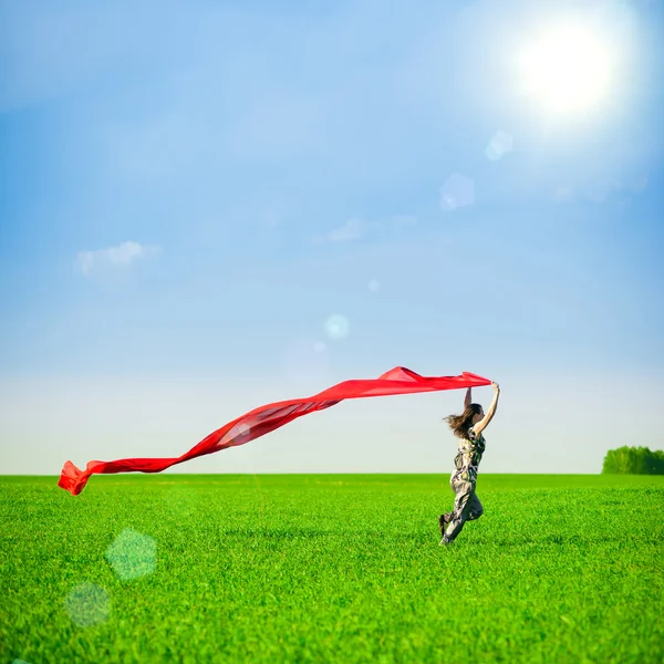 Beautiful young woman jumping on a green meadow with colored tissue — Stock Photo, Image