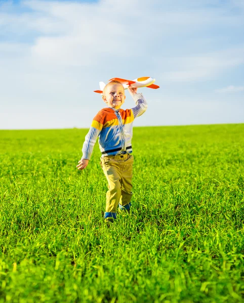 Happy boy playing with toy airplane against blue summer sky and green field background. — Stock Photo, Image