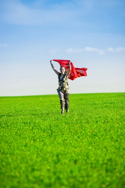 Beautiful young woman jumping on a green meadow with colored tissue — Stock Photo, Image