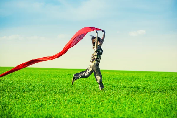 Mulher bonita pulando em um prado verde com tecido colorido — Fotografia de Stock