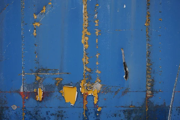 Blue metal container wall sheet with scratches and paint peeling off revealing yellow paint