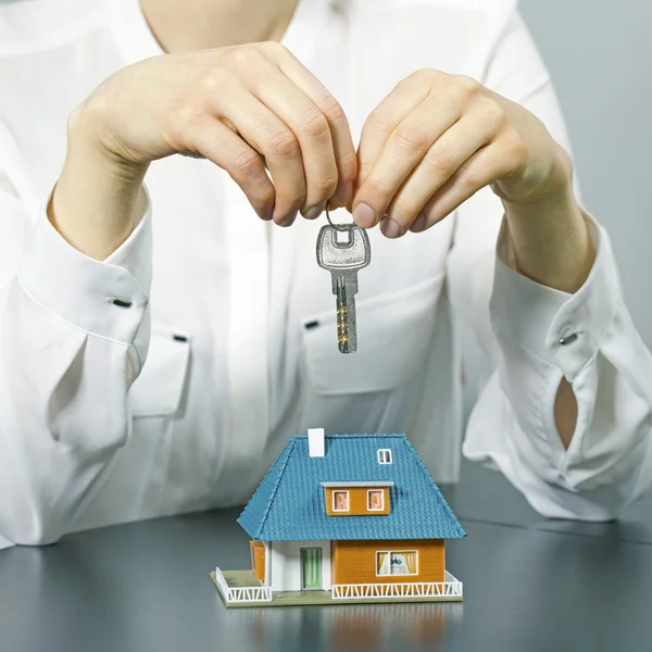 Real estate agent holding key above small house model on the tab — Stock Photo, Image