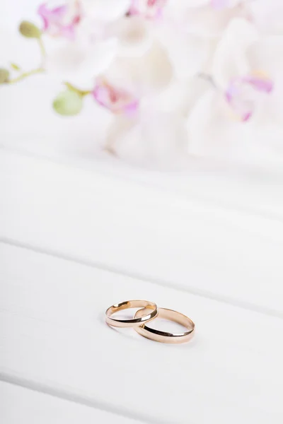 Golden wedding rings with flowers on white wooden table — Stock Photo, Image